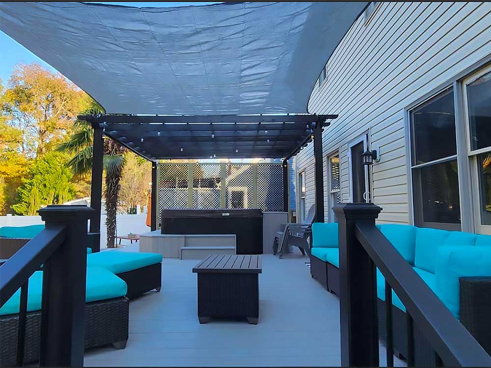 A spacious outdoor deck with turquoise seating and a modern pergola, showcasing professional craftsmanship in a backyard transformation. The deck installation features durable materials for a high-quality, low-maintenance outdoor living space.| First In Decks and Fencing | Virginia Beach Deck Builders