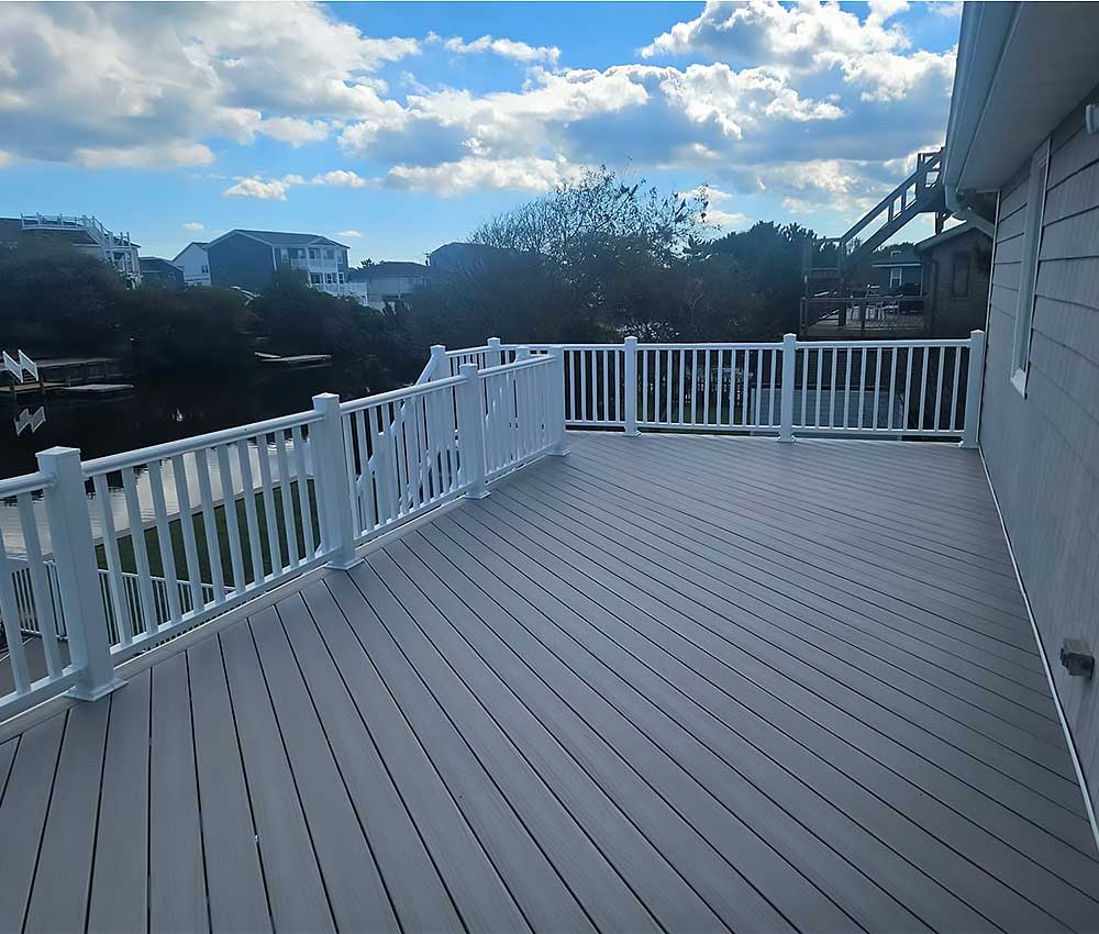A spacious, light gray composite decking with white railings offers an elegant outdoor living area, exemplifying professional craftsmanship and high-quality materials, ideal for backyard transformation projects in Virginia Beach.| First In Decks and Fencing | Virginia Beach Deck Builders