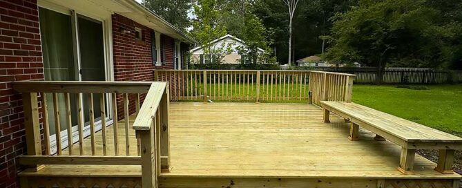 A newly constructed wooden deck with railing and built-in bench, showcasing professional craftsmanship using durable materials for outdoor living, set against a lush green backyard.| First In Decks and Fencing | Virginia Beach Deck Builders