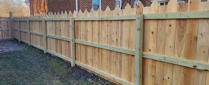 A newly installed wooden fence made from pressure treated lumber surrounds a backyard, showcasing professional craftsmanship and durable materials, ideal for enhancing outdoor living in Virginia Beach.| First In Decks and Fencing | Virginia Beach Deck Builders