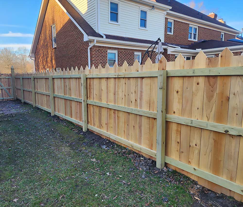 A newly installed wooden fence made from pressure treated lumber surrounds a backyard, showcasing professional craftsmanship and durable materials, ideal for enhancing outdoor living in Virginia Beach.| First In Decks and Fencing | Virginia Beach Deck Builders