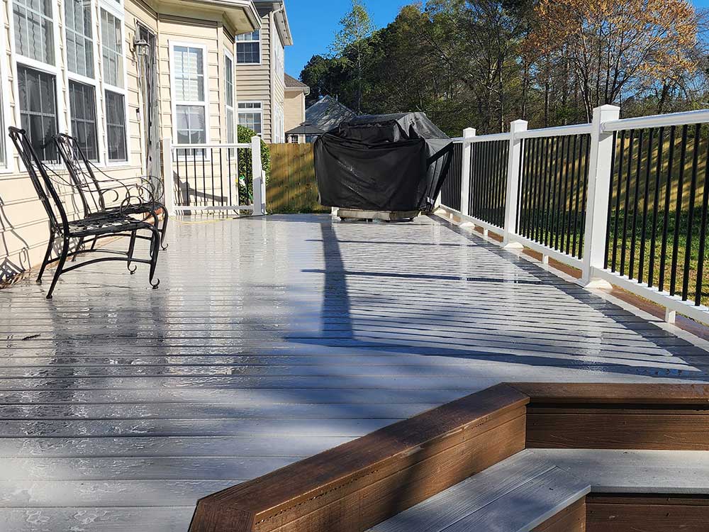 A spacious backyard deck features glossy composite decking with white railings and a black grill cover, exemplifying high-quality deck installation for outdoor living in Virginia Beach. A black metal bench rests against the house.| First In Decks and Fencing | Virginia Beach Deck Builders