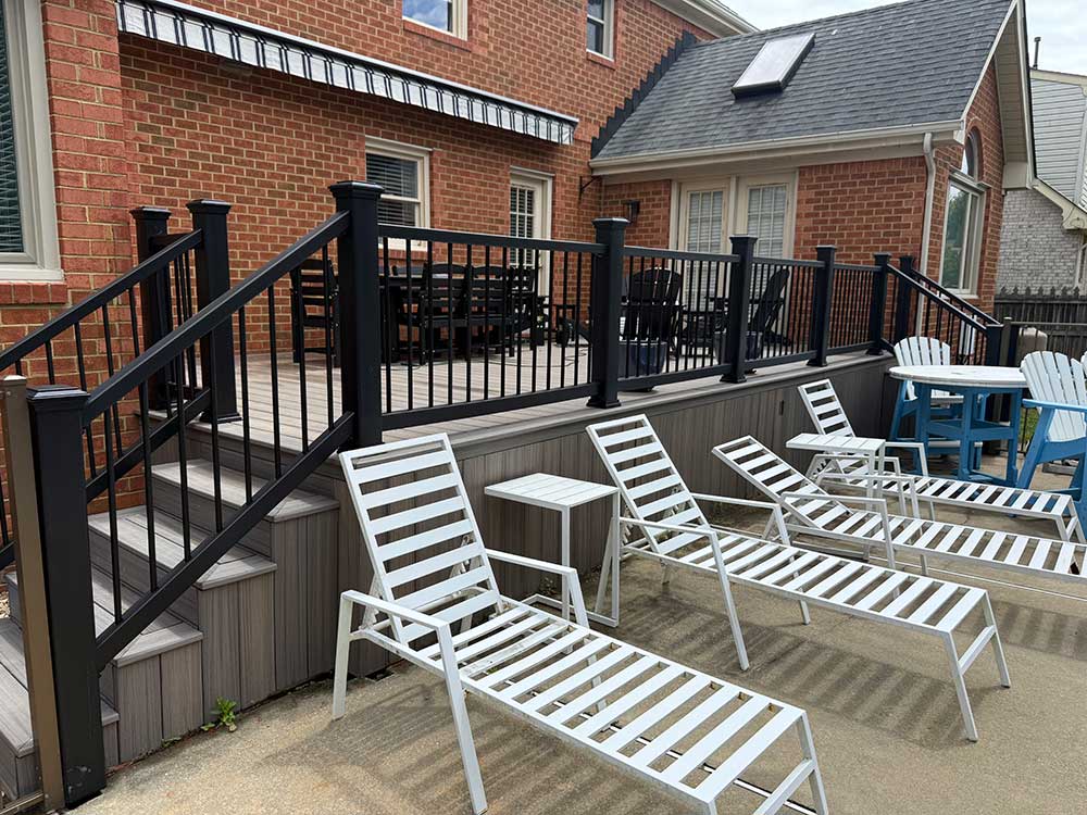 A spacious backyard features a custom deck installation with black railings and composite decking, surrounded by white lounge chairs, offering a stylish outdoor living space perfect for relaxation and home improvement in Chesapeake.| First In Decks and Fencing | Virginia Beach Deck Builders