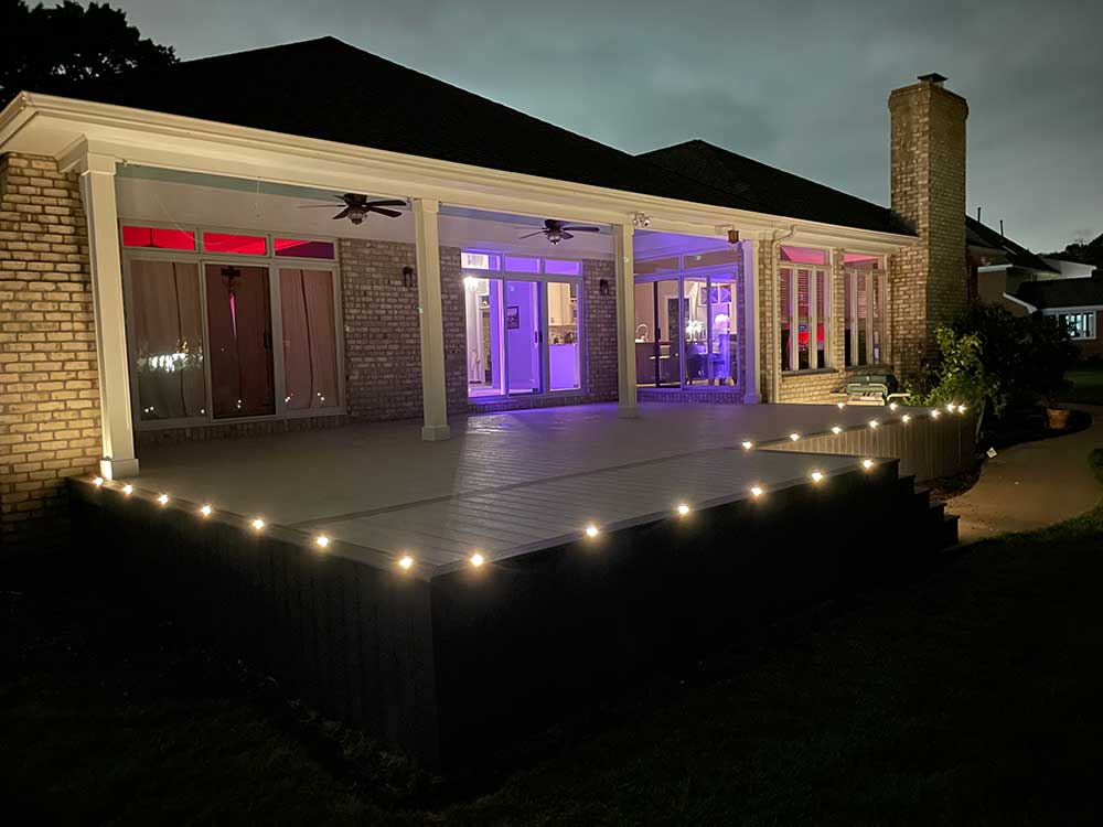 A beautifully illuminated custom deck installation with built-in lights enhances the outdoor living space of a brick home, showcasing professional craftsmanship and high-quality, durable materials for a stunning backyard transformation.| First In Decks and Fencing | Virginia Beach Deck Builders