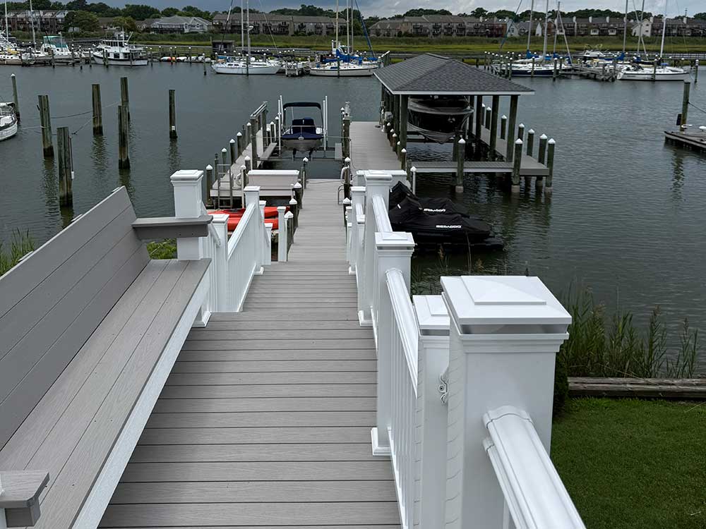 A scenic dock featuring custom decks with white railings overlooks a calm marina. The composite decking leads to a boat slip, showcasing the high-quality, durable materials used for outdoor living enhancements.| First In Decks and Fencing | Virginia Beach Deck Builders