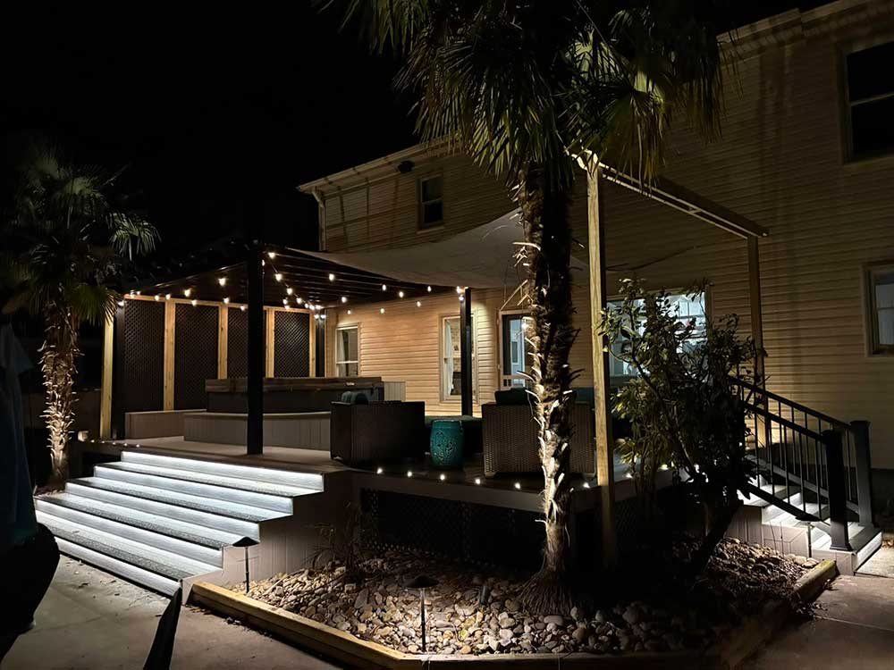 A beautifully lit deck with steps, featuring a pergola and cozy seating area, showcases professional craftsmanship and custom decks, perfect for outdoor living in Virginia…| First In Decks and Fencing | Virginia Beach Deck Builders