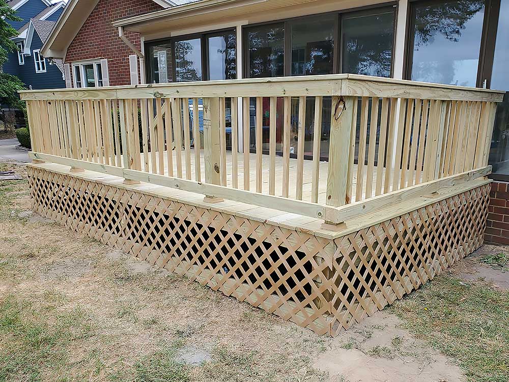 A newly constructed wooden deck with lattice skirting is attached to a brick house, showcasing professional craftsmanship and high-quality, durable materials, ideal for enhancing outdoor living spaces in Chesapeake and Virginia Beach.| First In Decks and Fencing | Virginia Beach Deck Builders