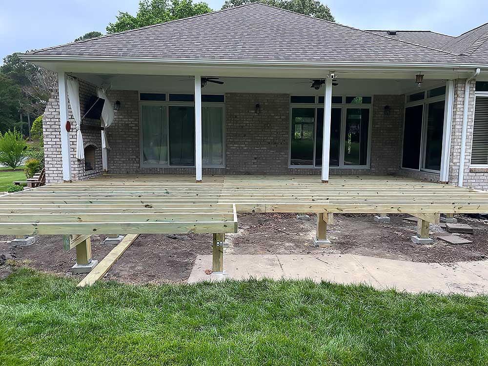A partially constructed deck extends from a brick house, showcasing professional craftsmanship with pressure treated lumber, ideal for outdoor living and home improvement in Virginia Beach.| First In Decks and Fencing | Virginia Beach Deck Builders