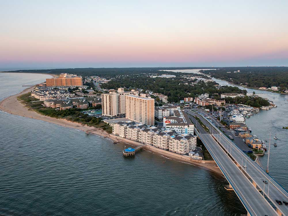 Aerial view of Virginia Beach's coastline with buildings and a bridge at sunset, showcasing potential sites for custom decks and outdoor living enhancements using high-quality, durable materials for a stunning backyard transformation.| First In Decks and Fencing | Virginia Beach Deck Builders