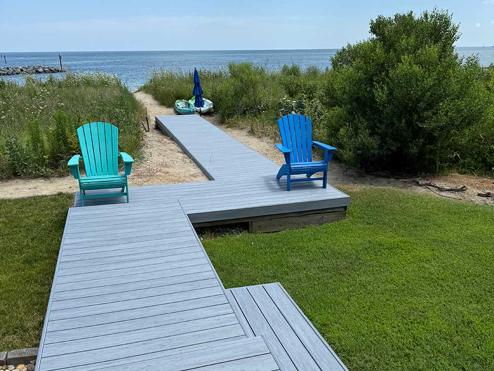 A scenic backyard features a custom deck installation with composite decking, two colorful Adirondack chairs, and a view of the ocean, highlighting the perfect outdoor living space with durable materials and professional craftsmanship.| First In Decks and Fencing | Virginia Beach Deck Builders