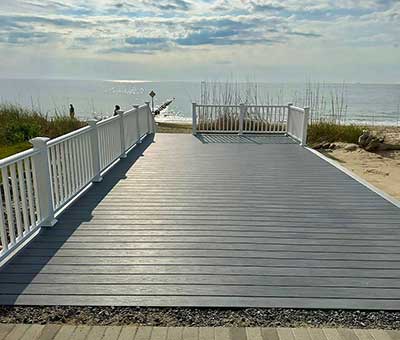A spacious, gray composite deck overlooking a beach, featuring white railings, exemplifies high-quality outdoor living and custom deck installation in Virginia Beach, with durable materials ideal for a low-maintenance lifestyle.| First In Decks and Fencing | Virginia Beach Deck Builders