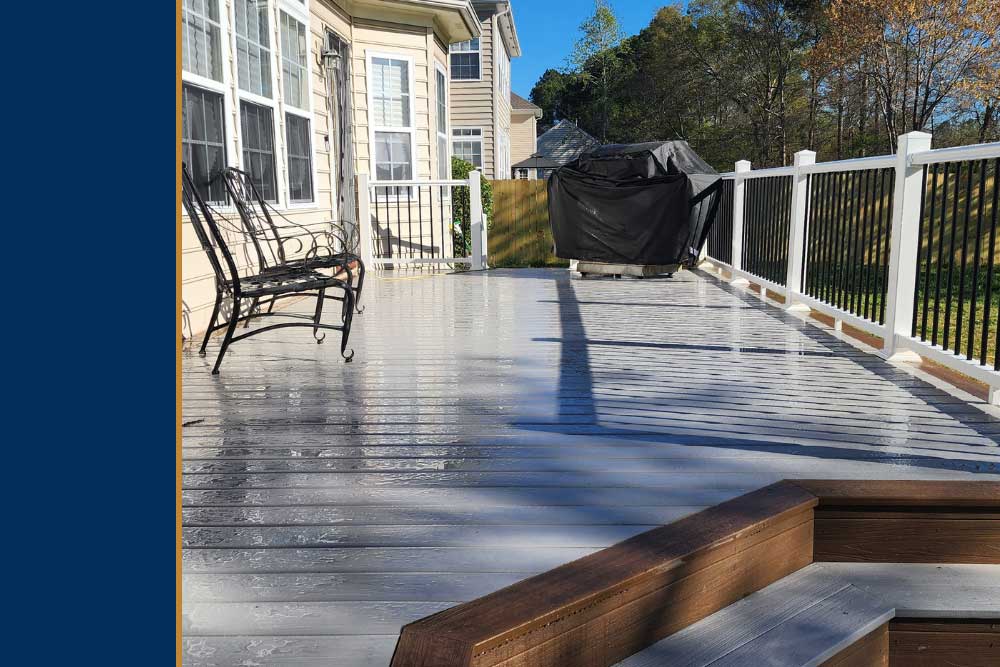A sunlit backyard deck made of high-quality composite decking features elegant black metal chairs and a grill, showcasing professional craftsmanship and an inviting outdoor living space.| First In Decks and Fencing | Virginia Beach Deck Builders