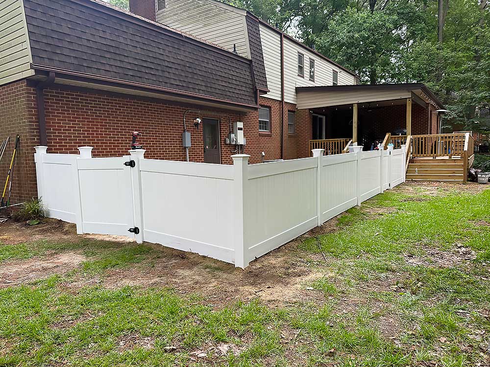 aluminum-and-vinyl-fences-1 White vinyl privacy fence installed around a backyard with a deck, offering security and aesthetic appeal.