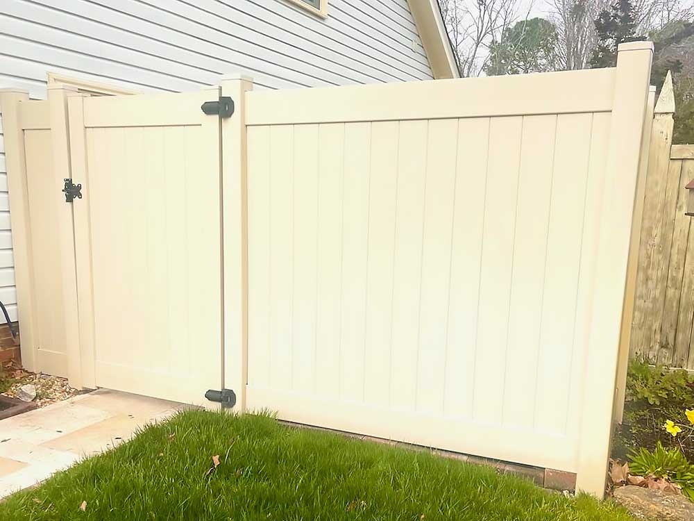 A beige vinyl fence stands tall in a backyard, showcasing professional craftsmanship and fence installation with high-quality, durable materials. The scene is set against a white house, highlighting the seamless home improvement.| First In Decks and Fencing | Virginia Beach Deck Builders