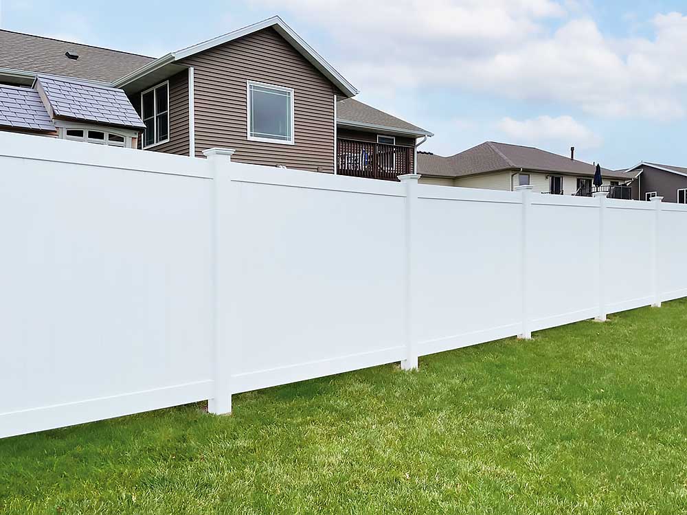 A pristine white vinyl fence encloses a suburban backyard, showcasing professional craftsmanship and high-quality, durable materials, ideal for enhancing outdoor living spaces in Chesapeake.| First In Decks and Fencing | Virginia Beach Deck Builders