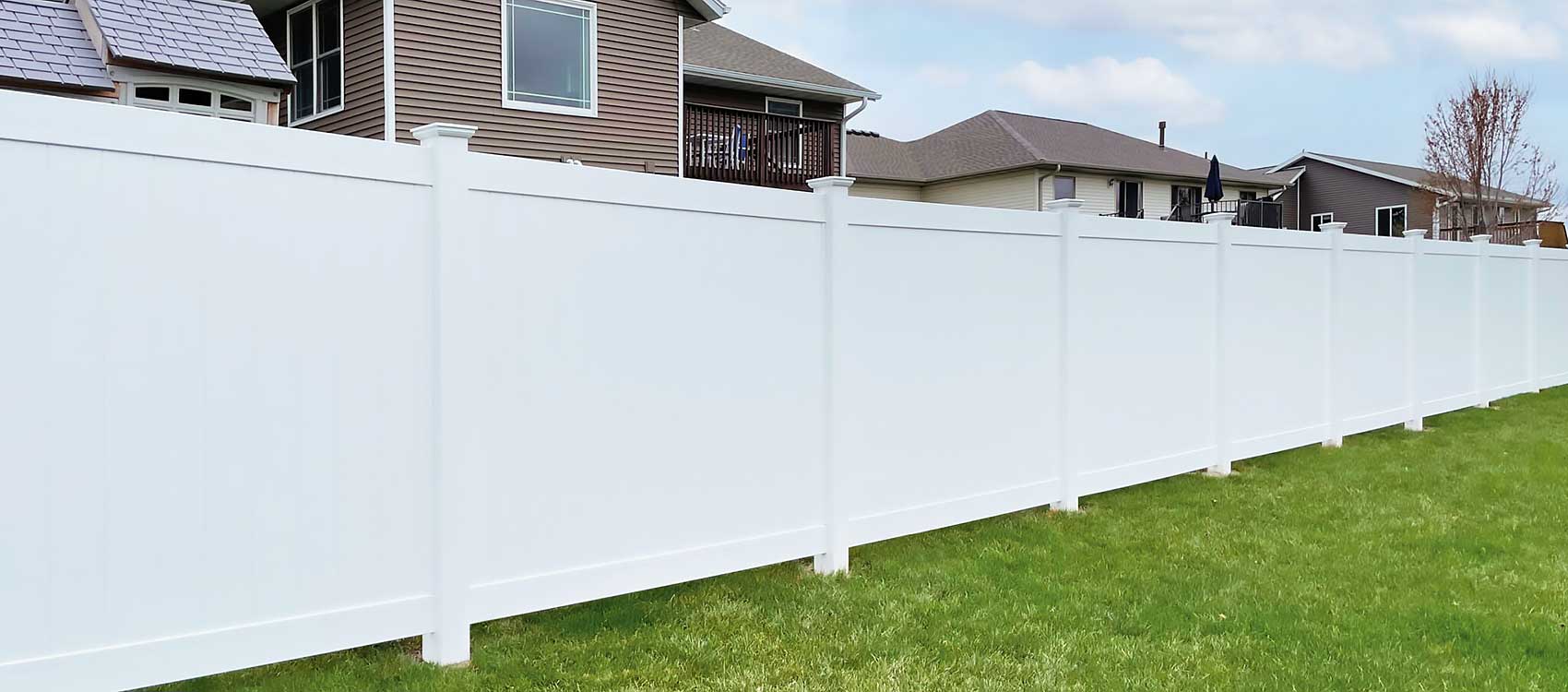 aluminum-and-vinyl-fences-long A white vinyl fence borders a lush green yard with houses in the background, showcasing professional craftsmanship and durable materials for a high-quality fence installation in outdoor living spaces.| First In Decks and Fencing | Virginia Beach Deck Builders
