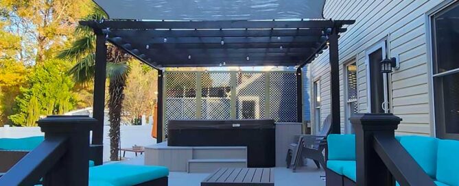 A spacious backyard deck in Virginia Beach features a pergola, comfortable seating with blue cushions, and a hot tub, showcasing high-quality, low-maintenance outdoor living with a focus on professional craftsmanship and backyard transformation.| First In Decks and Fencing | Virginia Beach Deck Builders