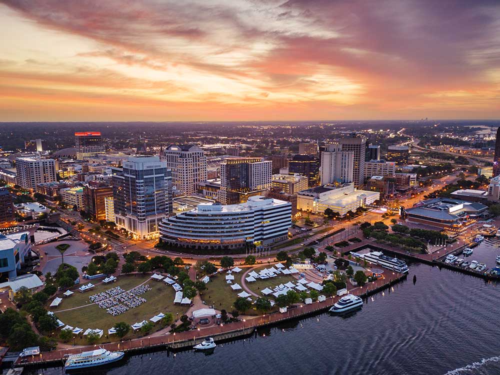 Aerial view of Norfolk at sunset, showcasing the vibrant cityscape with illuminated buildings and waterfront, ideal for outdoor living enhancements like custom decks and pergolas.| First In Decks and Fencing | Virginia Beach Deck Builders