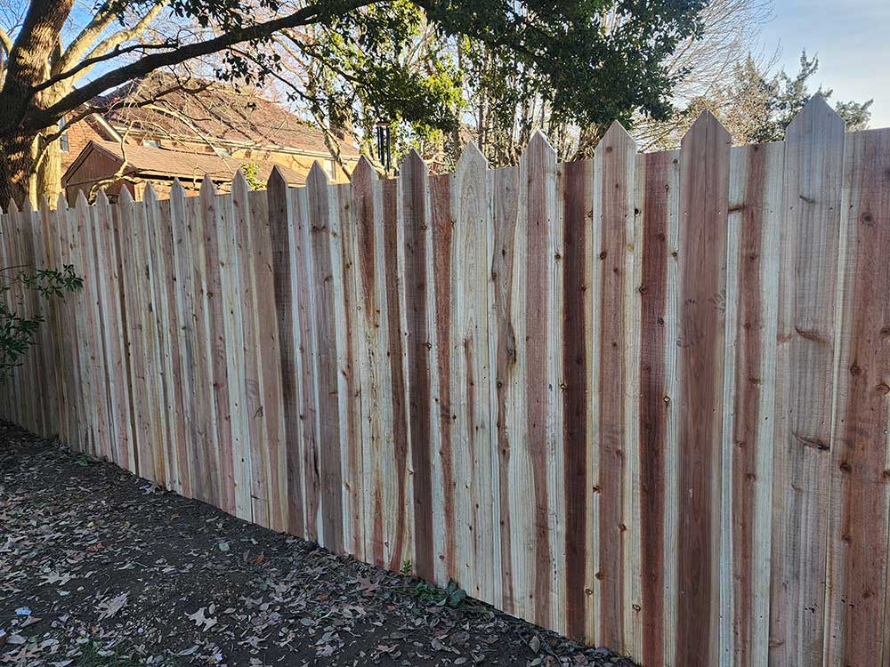 A tall wooden fence, made from durable materials, stands in a backyard, providing privacy and showcasing professional craftsmanship in fence installation.| First In Decks and Fencing | Virginia Beach Deck Builders