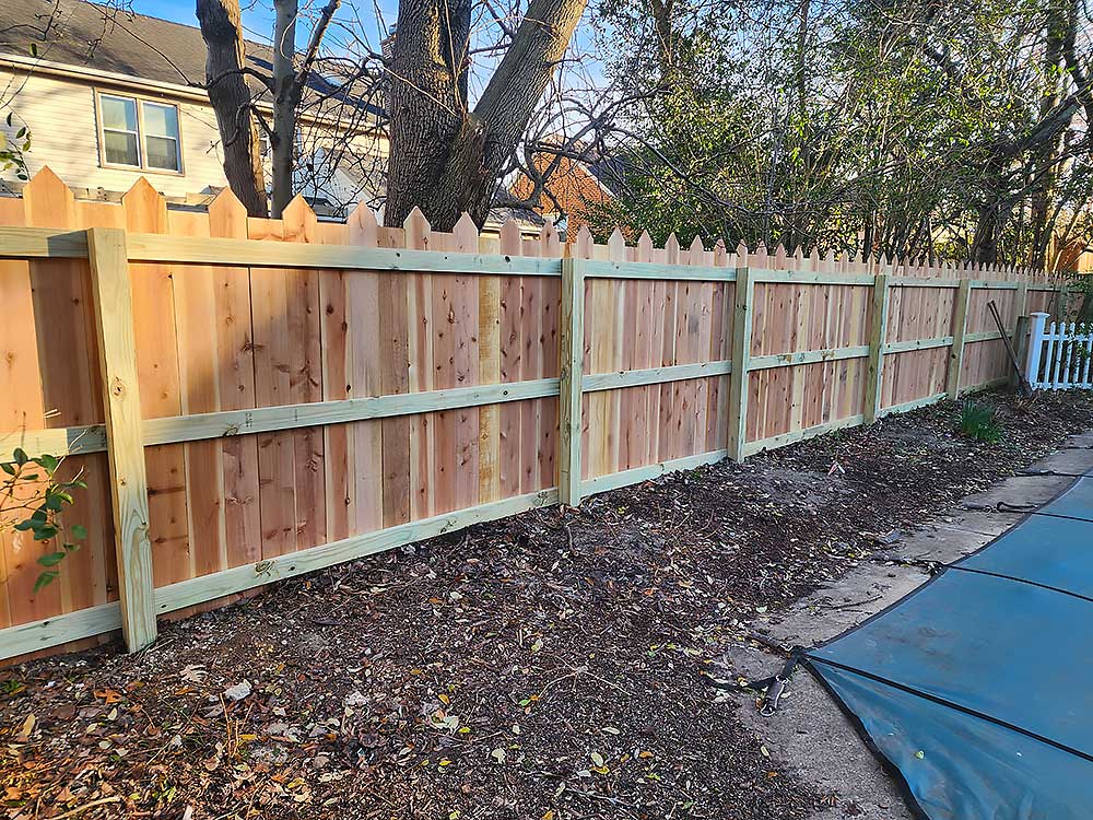 A newly installed wooden fence made of high-quality, durable materials stands in a backyard, providing privacy and enhancing outdoor living. The fence showcases professional craftsmanship, ideal for home improvement projects in Chesapeake.| First In Decks and Fencing | Virginia Beach Deck Builders
