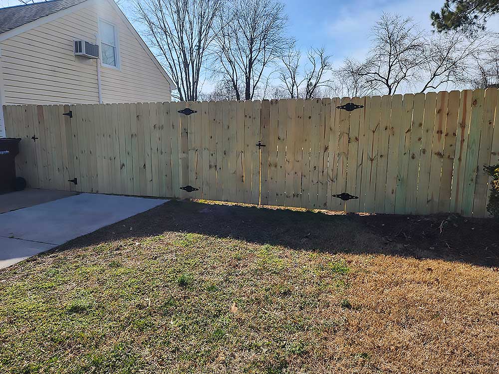 A newly installed wooden fence stands in a backyard, showcasing high-quality craftsmanship and durable materials, perfect for outdoor living enhancements in Chesapeake.| First In Decks and Fencing | Virginia Beach Deck Builders