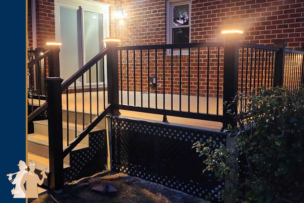 A well-lit custom deck with black railings and steps leads to a brick house, showcasing professional craftsmanship and high-quality, durable materials, ideal for enhancing outdoor living spaces in Virginia Beach.| First In Decks and Fencing | Virginia Beach Deck Builders